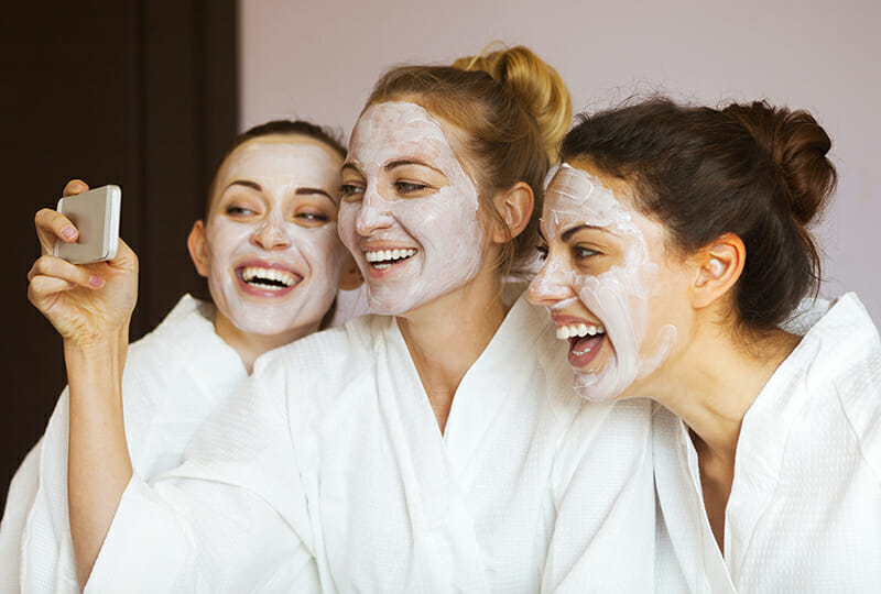 Three young happy women with face masks taking selfie at spa resort. Friendship and wellbeing concept